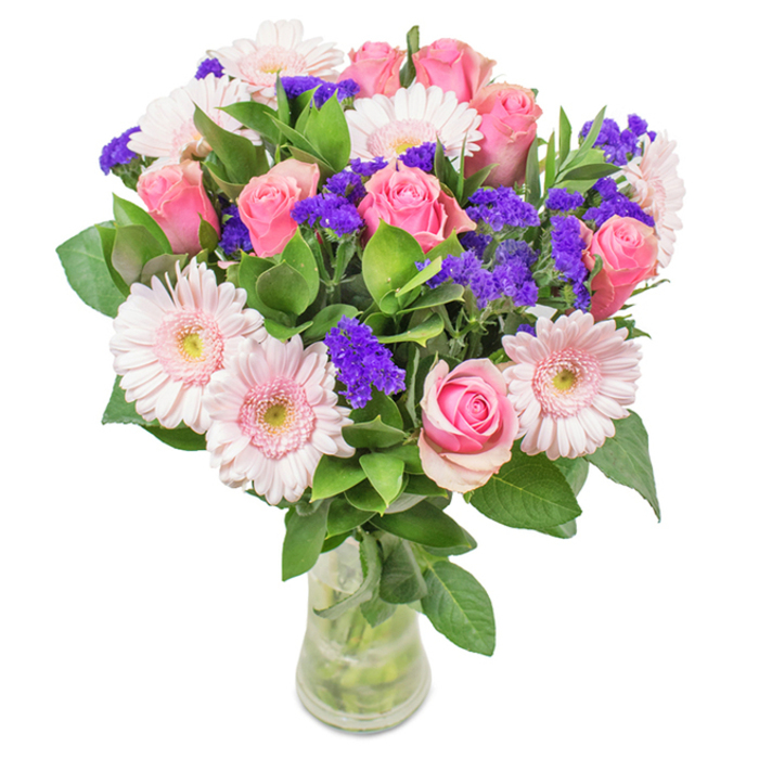 Vivid and elegantly composed, this floral bouquet is carefully assembled in a transparent glass vase, displaying its stems and clear water in an inviting, honest fashion. The arrangement features a central cluster of roughly 7-9 soft and mid-pink roses, their petals in various stages of bloom, from lusciously furled buds to more open spirals-conveying the timeless grace of florals found in Hemel Hempstead gardens. They are harmoniously paired with 5-7 pale pink Gerbera daisies, each flower distinguished by luminous, rounded heads and almost snowy centres, invoking the freshness of spring along the Canal Walk. Intermixed throughout are pops of purple statice, lending texture, vibrancy, and contrast while evoking the wild beauty of nearby fields. The base is woven with rich, deep green foliage, enhancing visual depth and amplifying the bouquet's sense of abundance. Set against a pristine white background, the arrangement radiates freshness and celebration-a perfect choice for birthdays, anniversaries, Mother's Day, or a thoughtful decorative touch, reflecting the heartfelt spirit of Hemel Hempstead's flower community.